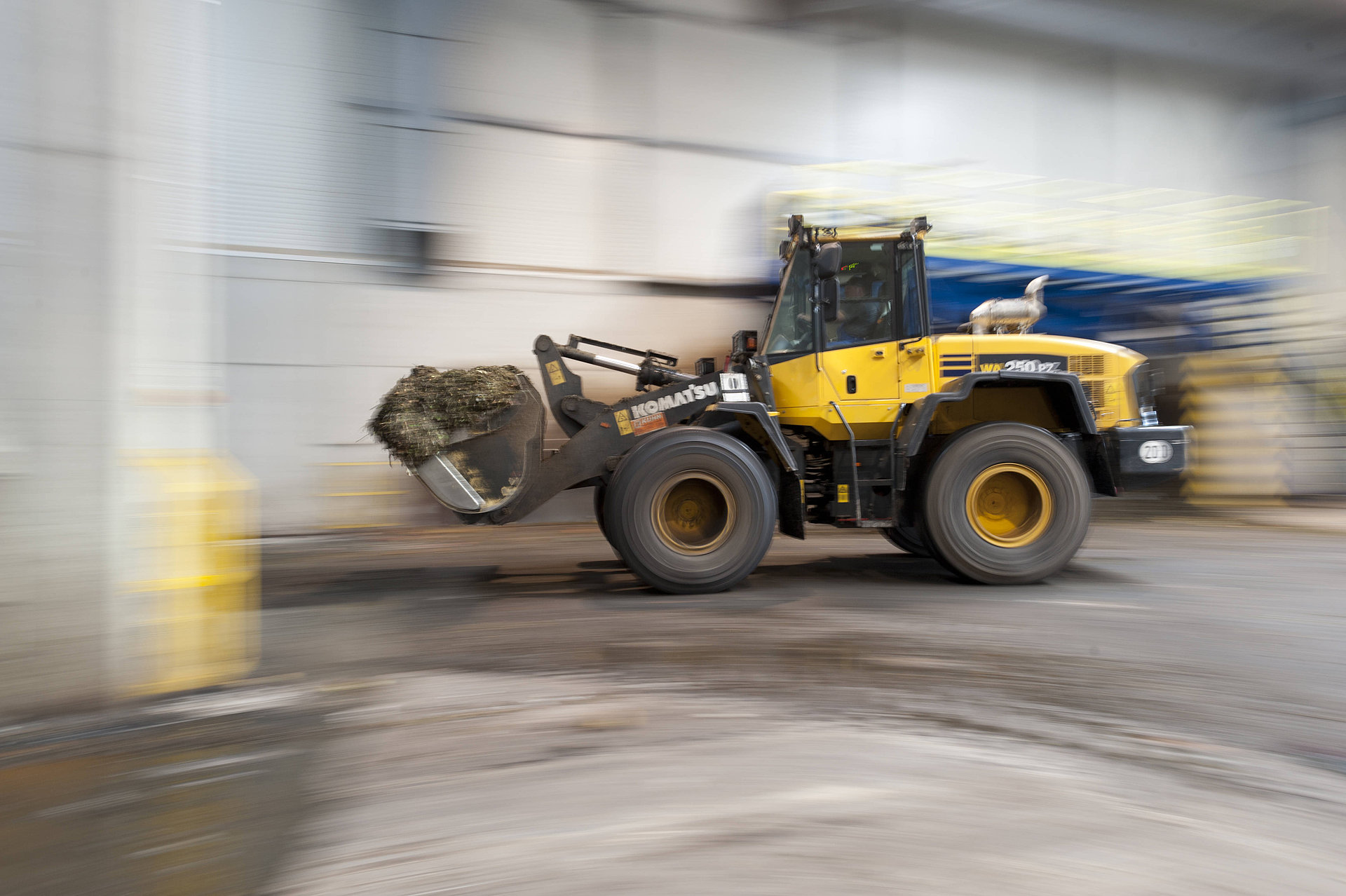 Gelber Radlader der Marke Komatsu transportiert organisches Material in einer Halle.