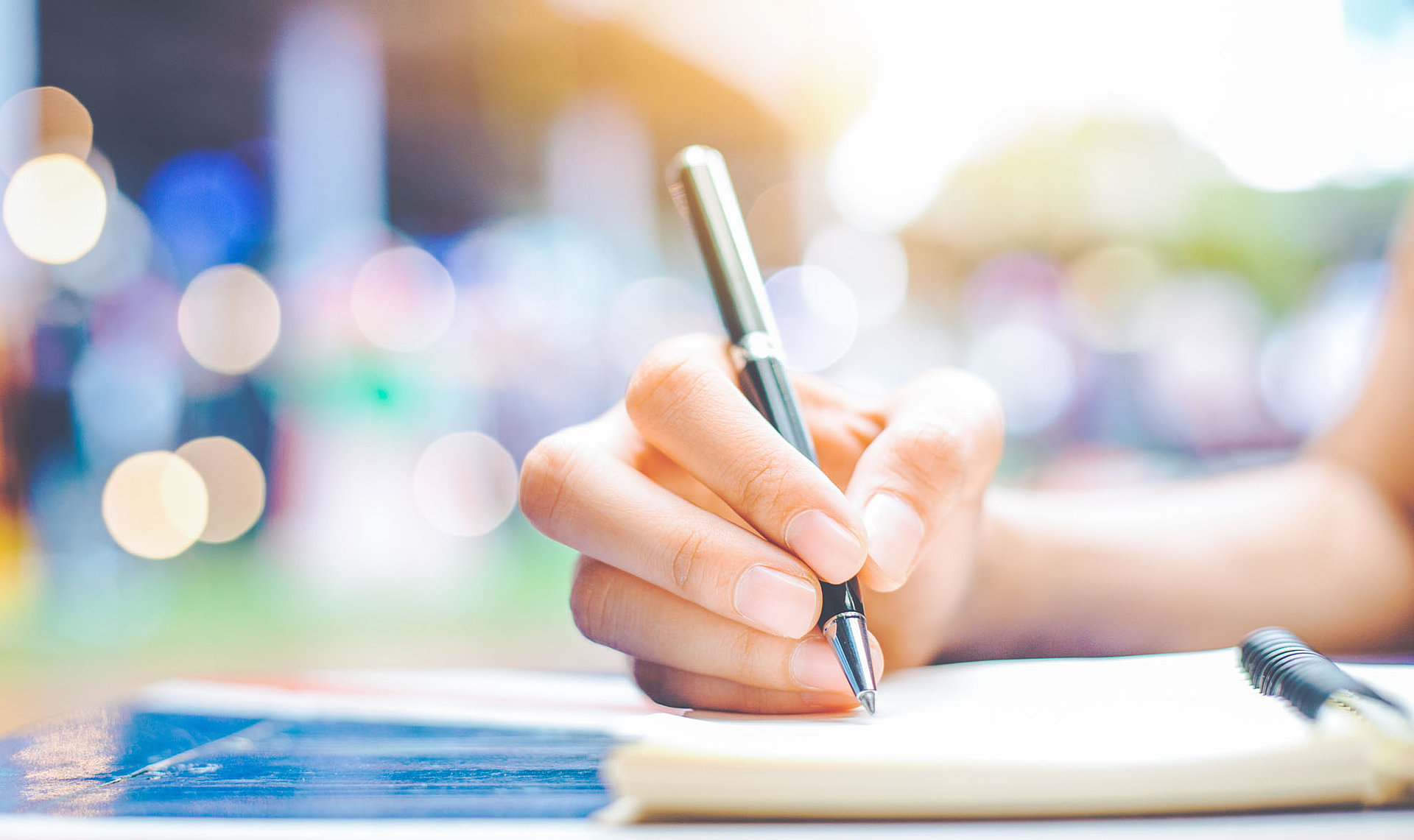 Nahaufnahme einer Hand, die mit einem Stift auf einem Klemmbrett Notizen macht. Das Bild symbolisiert die Verwaltung, Dokumentation oder die Bearbeitung von Gebührenveranlagungen.